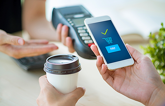 hands holding coffee and mobile phone making a point of sale payment