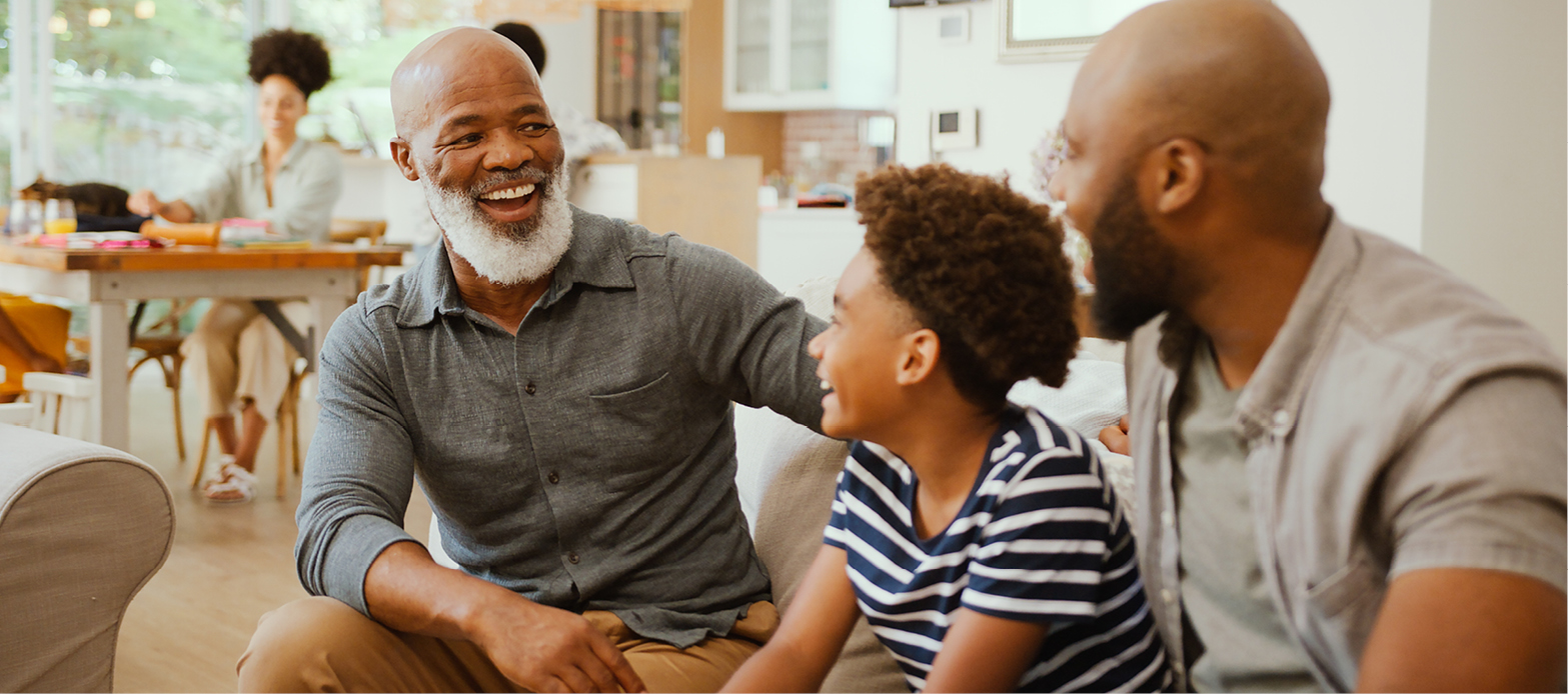 Three generations of men sitting on couch smiling.