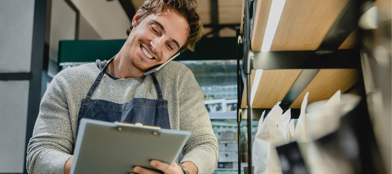 Small business owner smiles while writing on a clipboard and talking on the phone