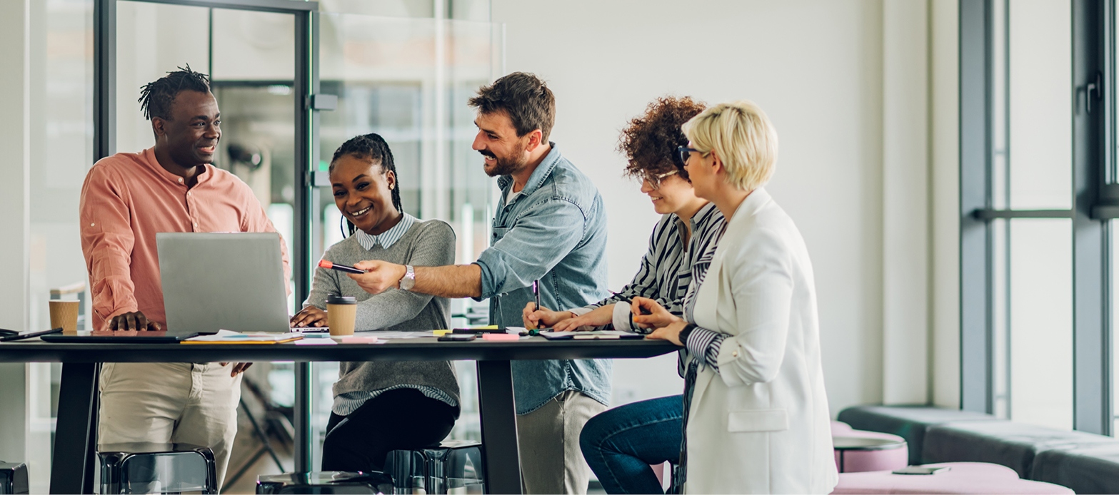 Diverse team stands around a desk collaborating on a project