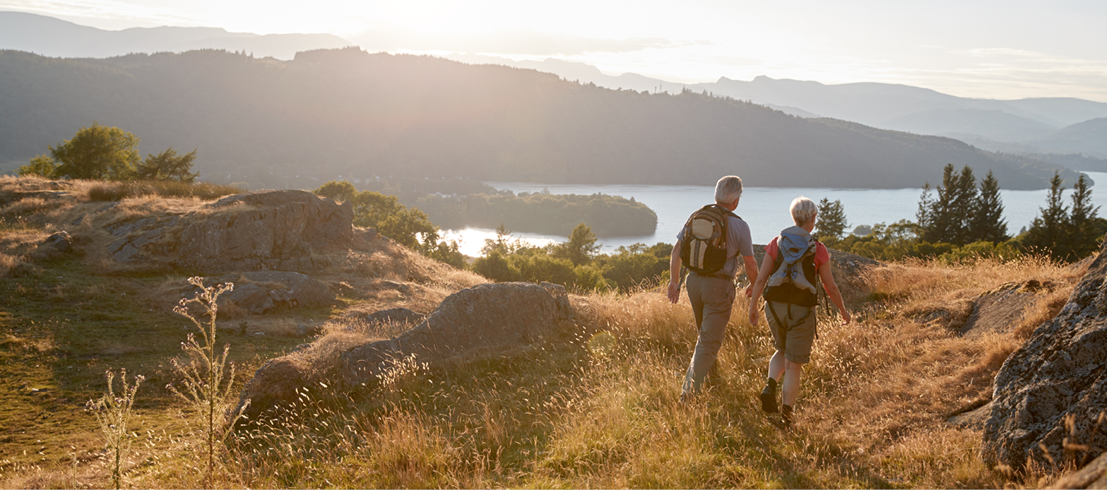 Couple hikes on trail in front of a lake and mountains