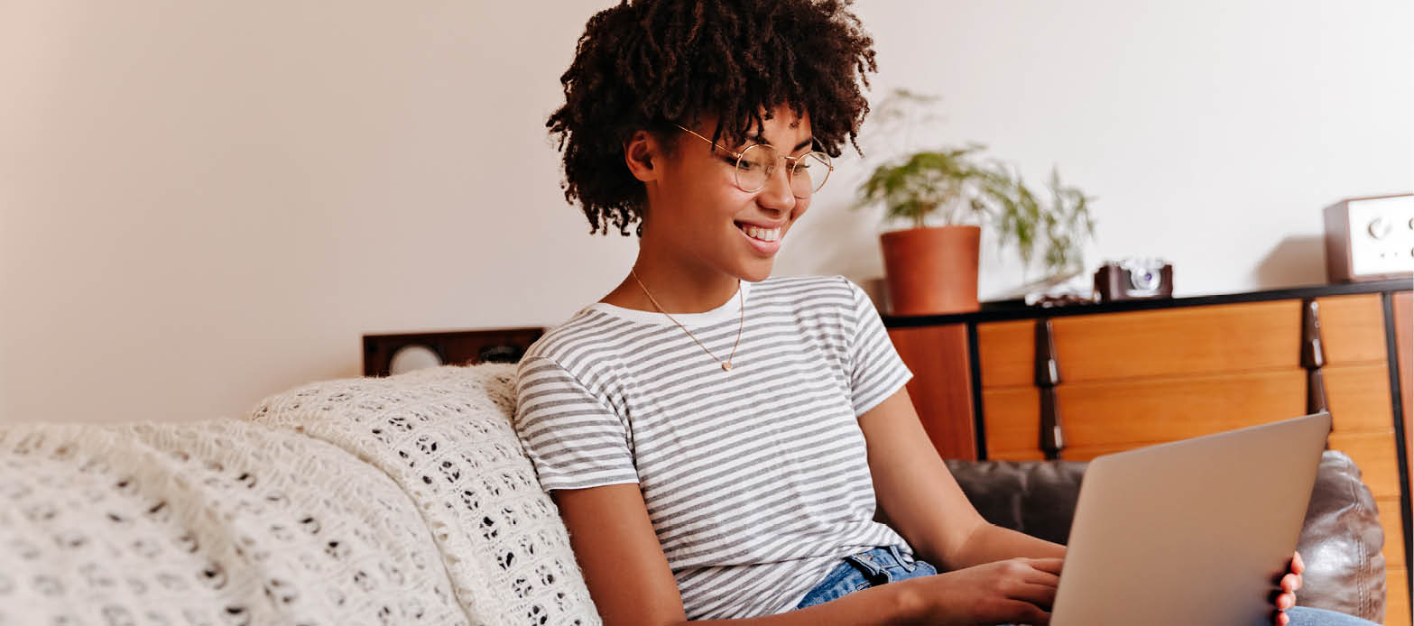 Teenager sits on the couch and smiles at laptop