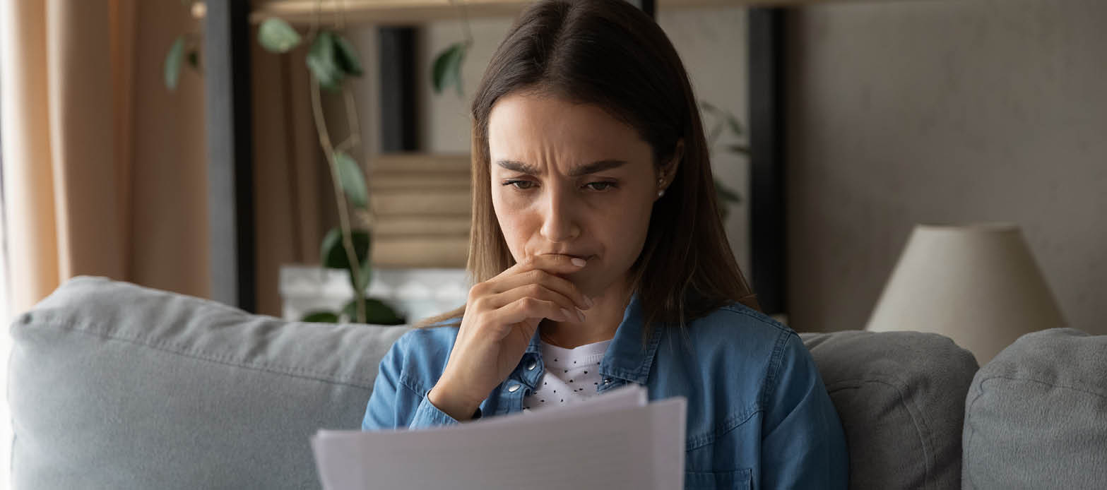 Woman looks worried while reviewing mail on the couch