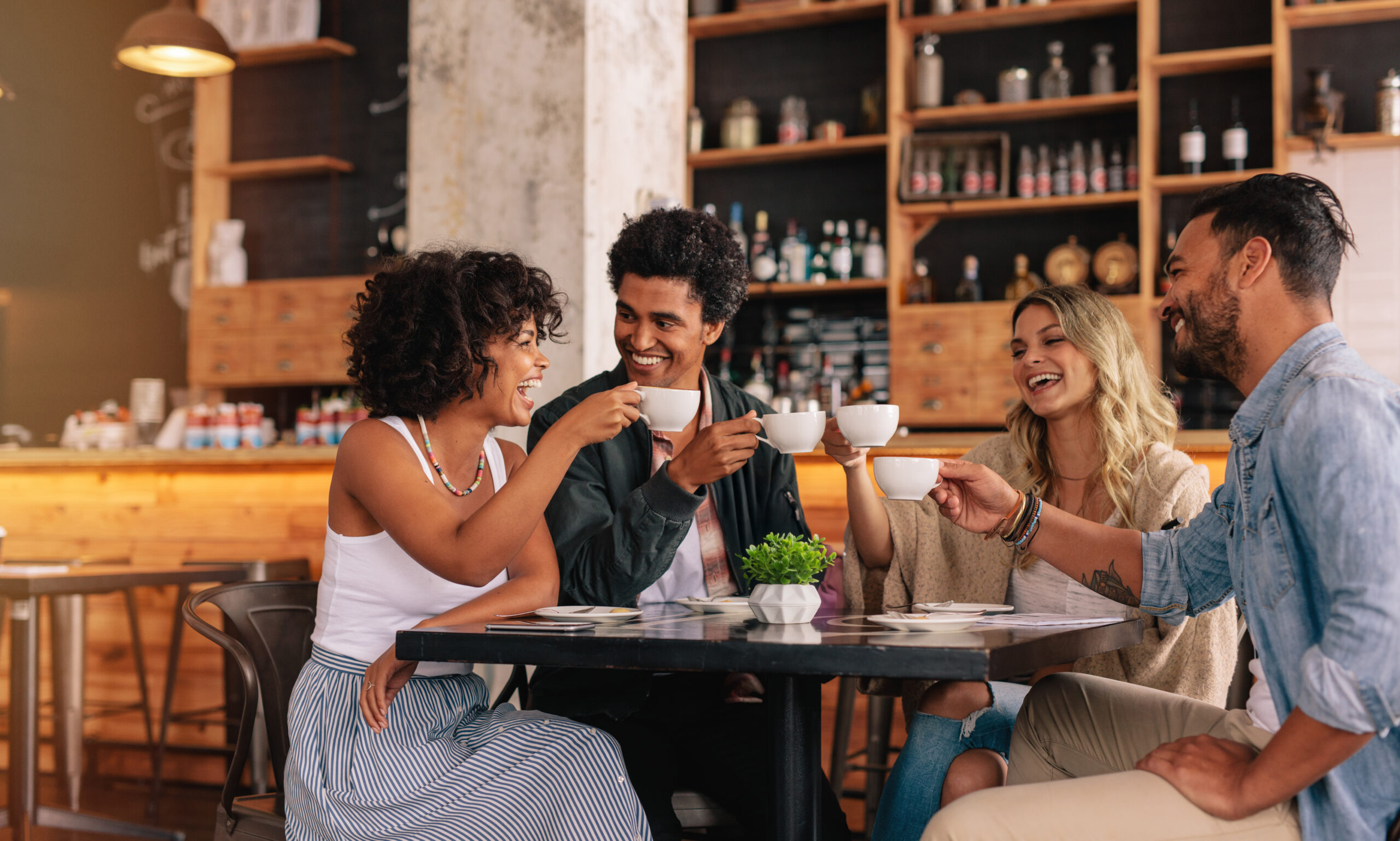 Four friends hold up their coffee mugs at a coffee shop