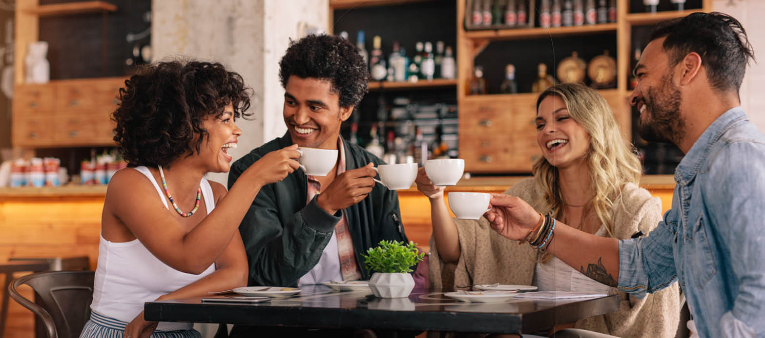 Four friends hold up their coffee mugs at a coffee shop
