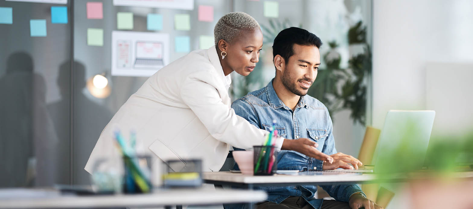 A woman and a man look at his laptop screen at his desk