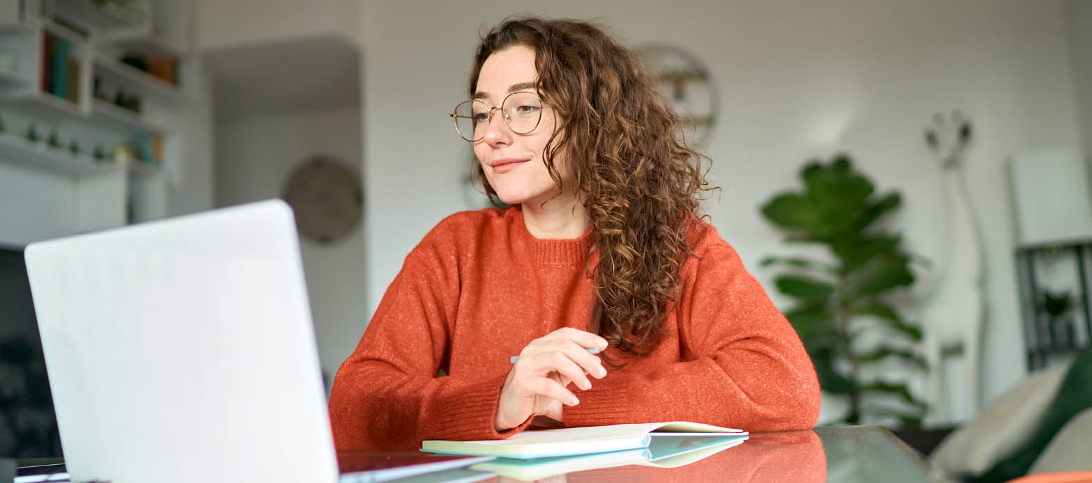 Woman looks at laptop while writing in a notebook