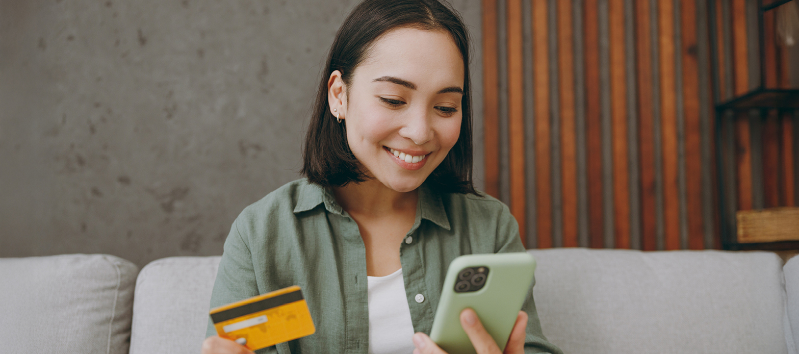 A woman is smiling while holding her phone and credit card