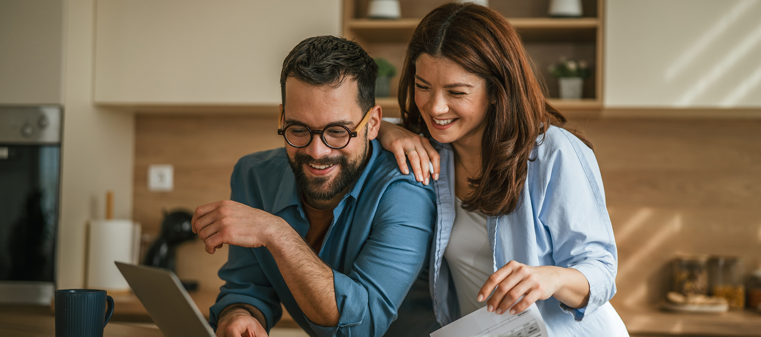 A man and a woman are both looking at a laptop smiling